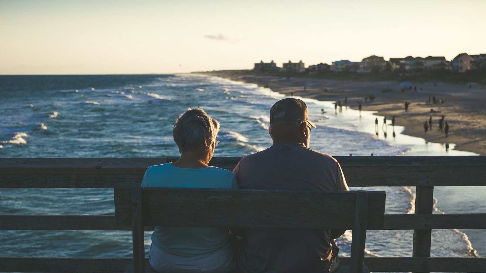 A retired couple sitting on a bench looking out at the beach